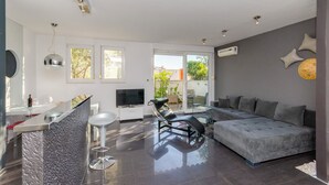 Un salón moderno con un sofá gris, una silla negra, una mesa de comedor de vidrio y un televisor.