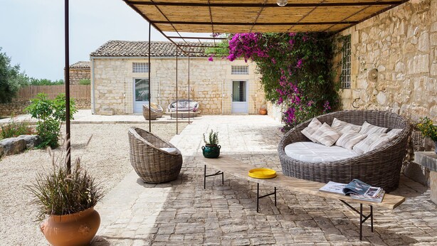 A covered outdoor seating area with wicker furniture, a stone wall, and a potted plant. - Luxury villa with pool near Scicli (Scicli)