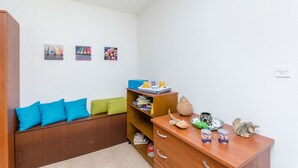 Una habitación con un banco de madera, un escritorio de madera con un florero, libros y objetos decorativos. Hay tres cuadros colgados en la pared y un interruptor de luz.