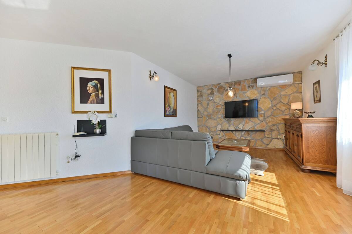 A living room with a grey sofa, a stone wall, a flat-screen TV, and a wooden cabinet.