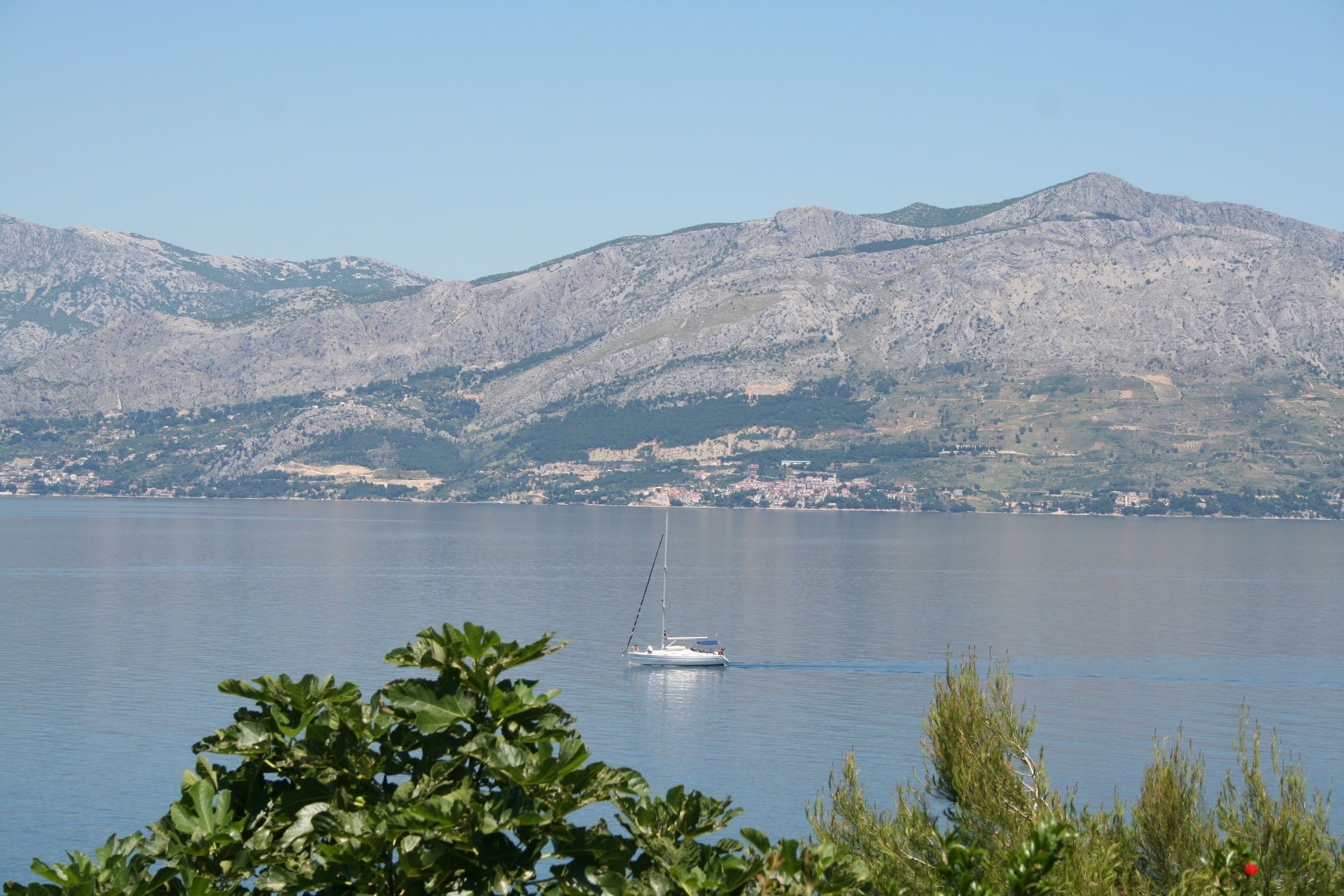 A calm lake with a sailboat, surrounded by mountains and greenery.