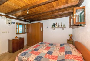 Een slaapkamer met een houten plafond, een bed met een lappendeken, een houten garderobe, een spiegel en een plank met flessen.