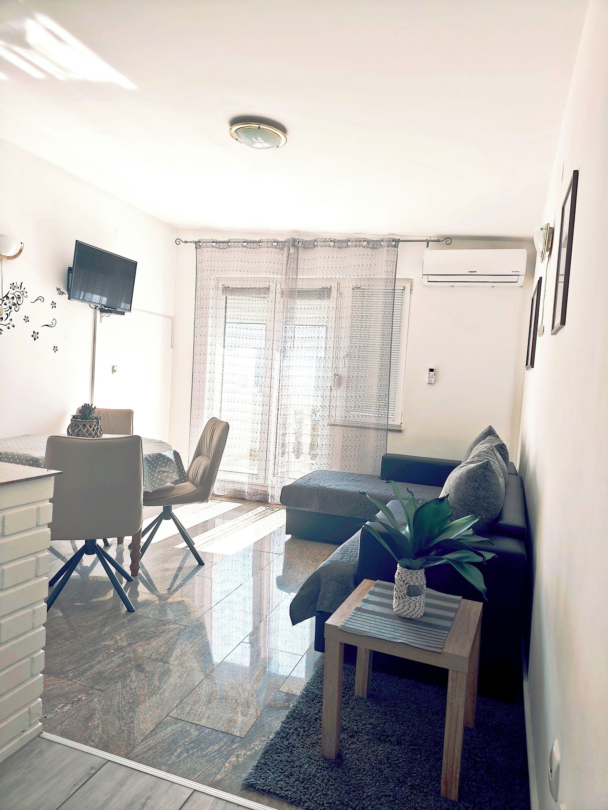 Un saló modern amb un televisor de pantalla plana fixat a la paret, un sofà, una taula de centre i una zona de menjador amb una cadira i una taula petita.
