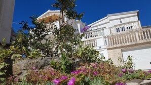 A white building with balconies and a garden with purple flowers. - Apartments Adriatic (Rogoznica)