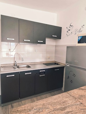 A modern kitchen with dark cabinets, a stainless steel sink, and a built-in oven. - Apartments Adriatic (Rogoznica)