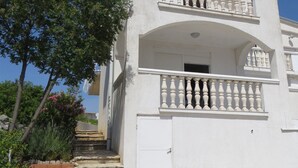 A two-story building with a white exterior, a balcony with balusters, and a stone staircase leading to the entrance. - Apartments Adriatic (Rogoznica)