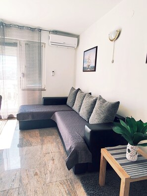 A modern living room with a sectional sofa, a small wooden table, and a potted plant. - Apartments Adriatic (Rogoznica)
