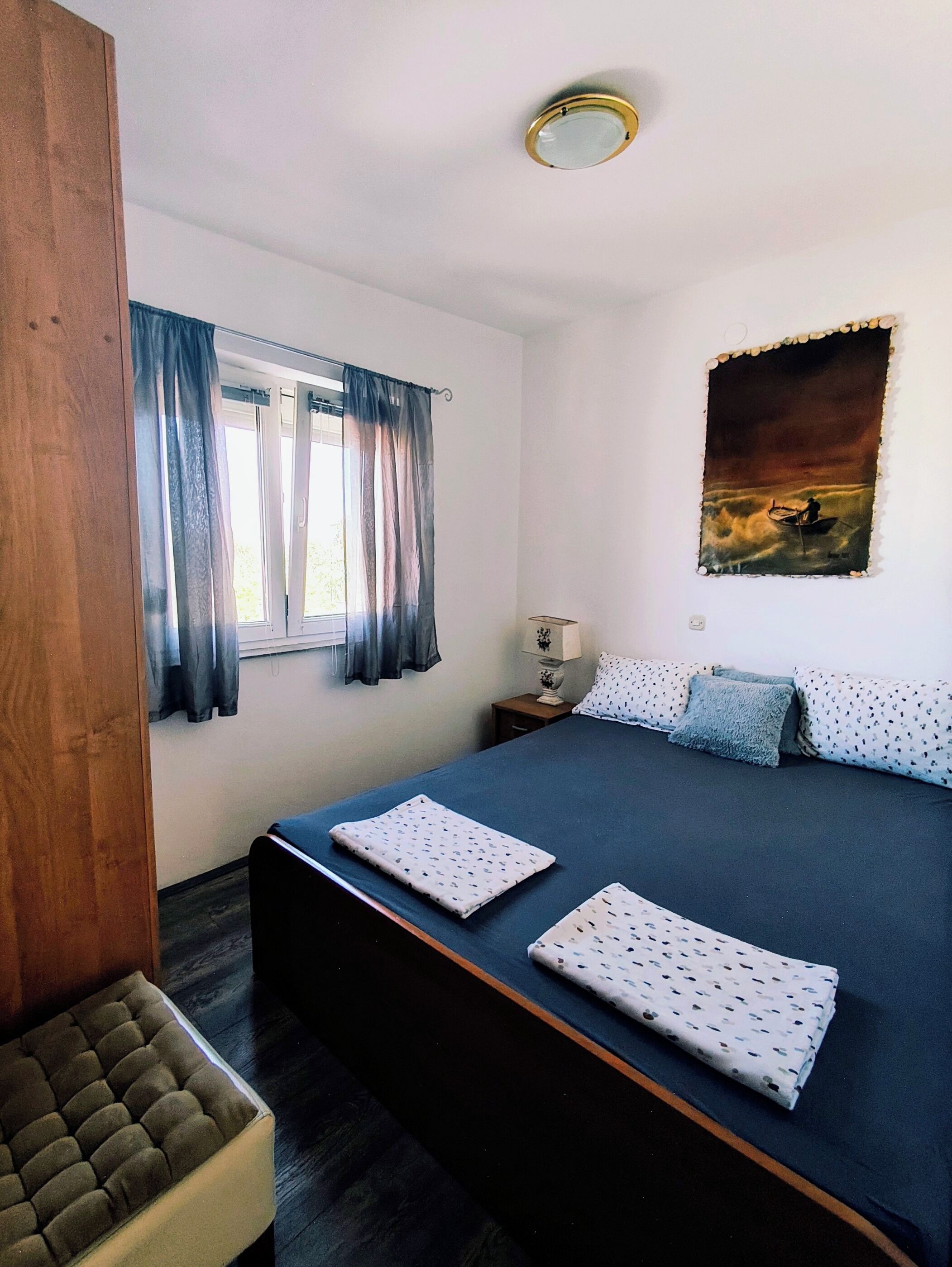 Um quarto com uma cama grande, uma mesa de cabeceira, uma luminária, uma janela com cortinas e um quadro na parede.