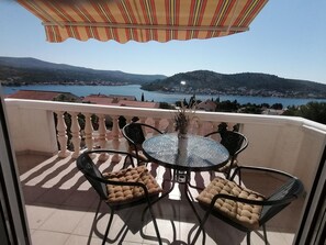 A balcony with a table and chairs, overlooking a lake and hills. - Apartments Adriatic (Rogoznica)