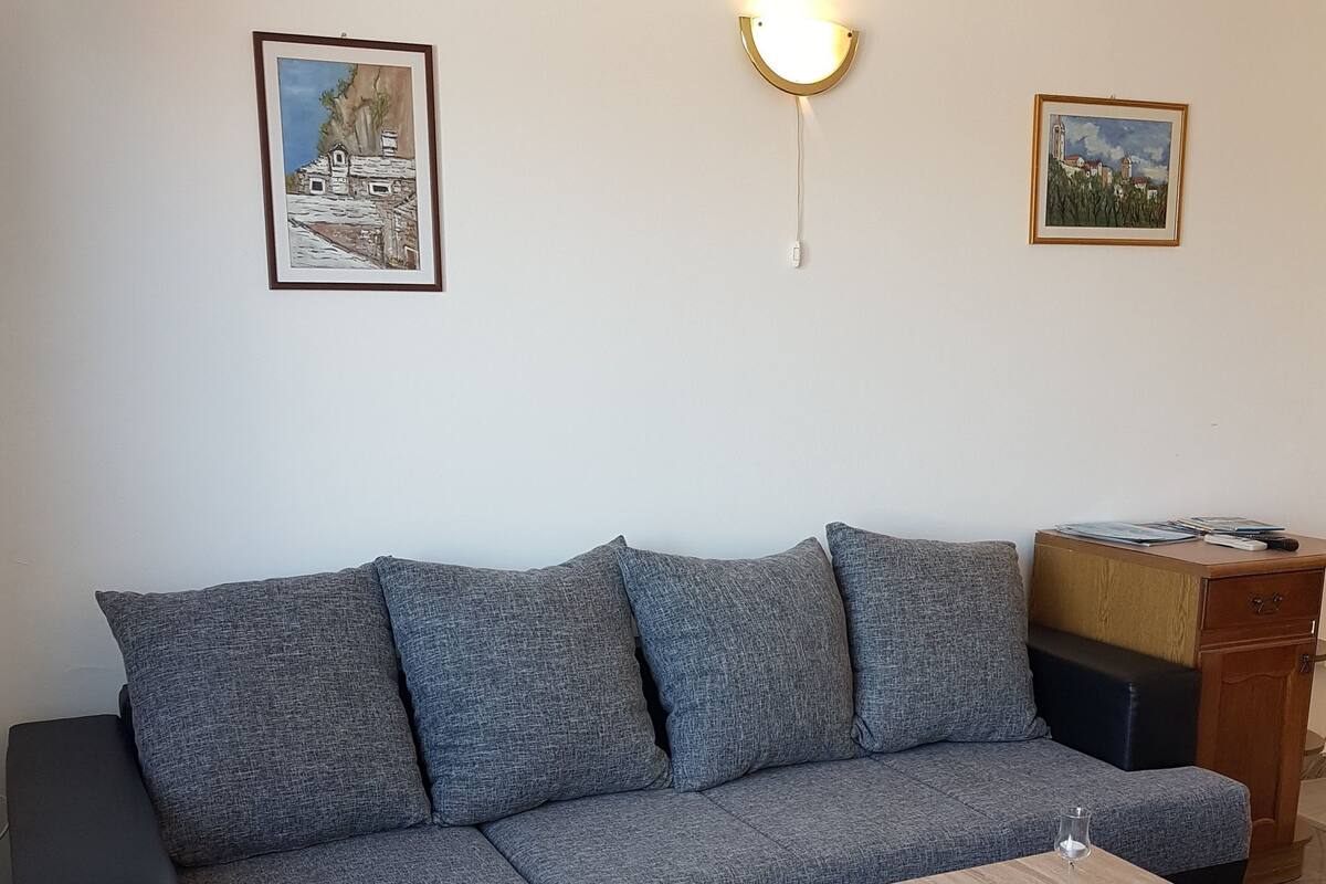 A modern living room with a grey sectional sofa, a small wooden coffee table, and two framed paintings on the wall.