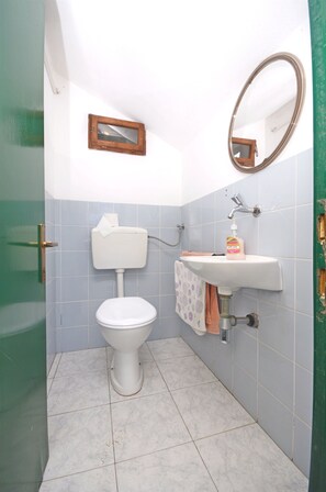 A bathroom with a toilet, sink, mirror, and tiled walls. - House Krunoslav (Postira)