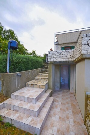 A stone-walled building with a small entrance and a tiled pathway leading to a door. - House Krunoslav (Postira)