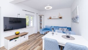 Una sala de estar moderna con un televisor de pantalla plana, un sofá azul, una mesa de comedor con sillas y un pequeño modelo de barco en un estante.