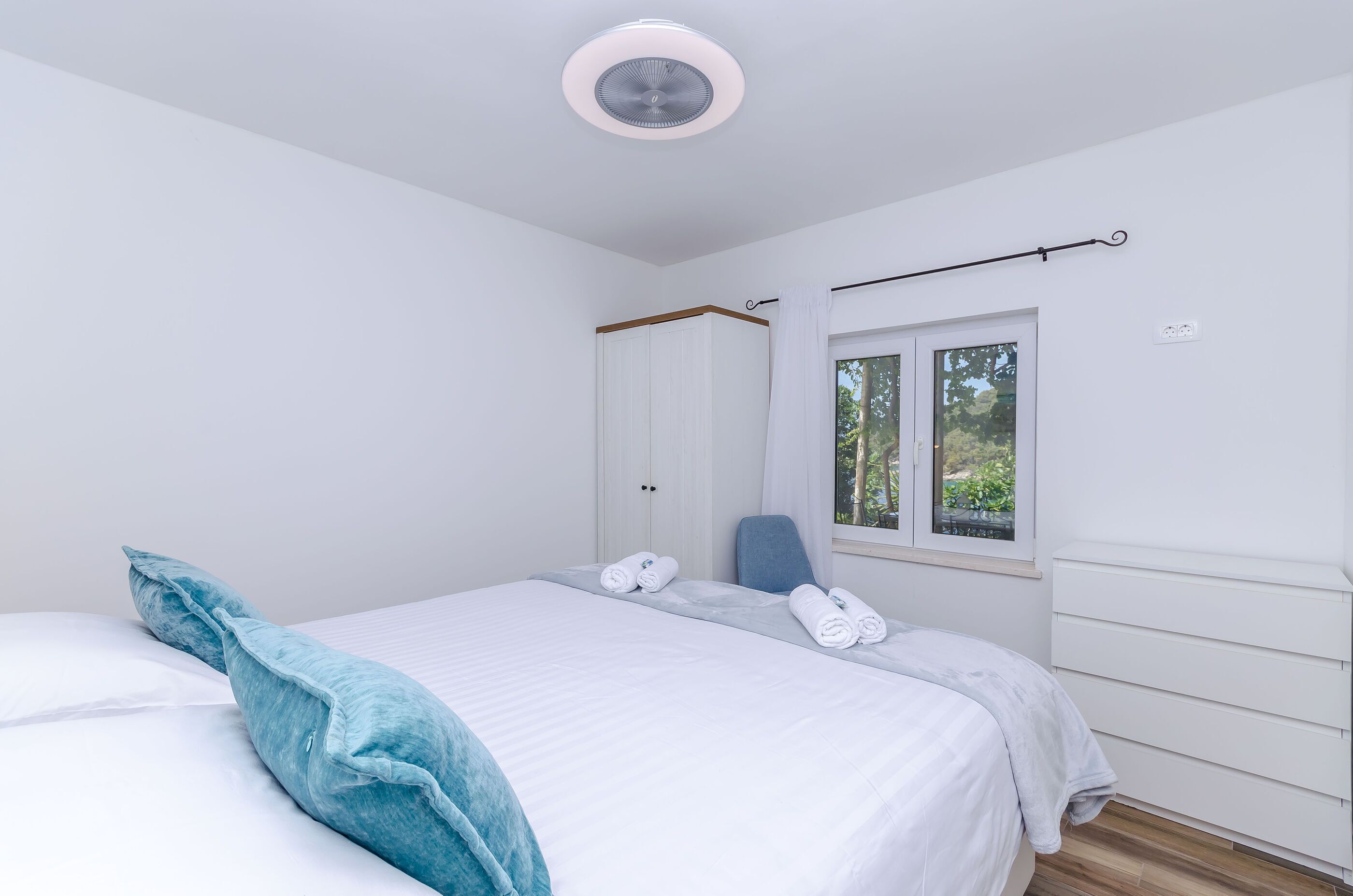 A bedroom with a bed, a chair, a wardrobe, a window, and a ceiling fan.