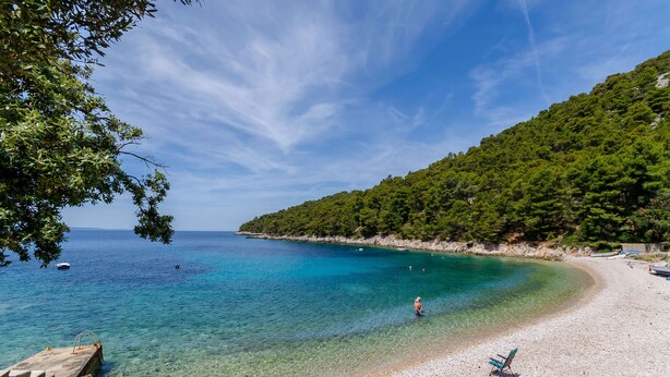 Una playa con aguas turquesas cristalinas, una costa rocosa y una colina boscosa al fondo.