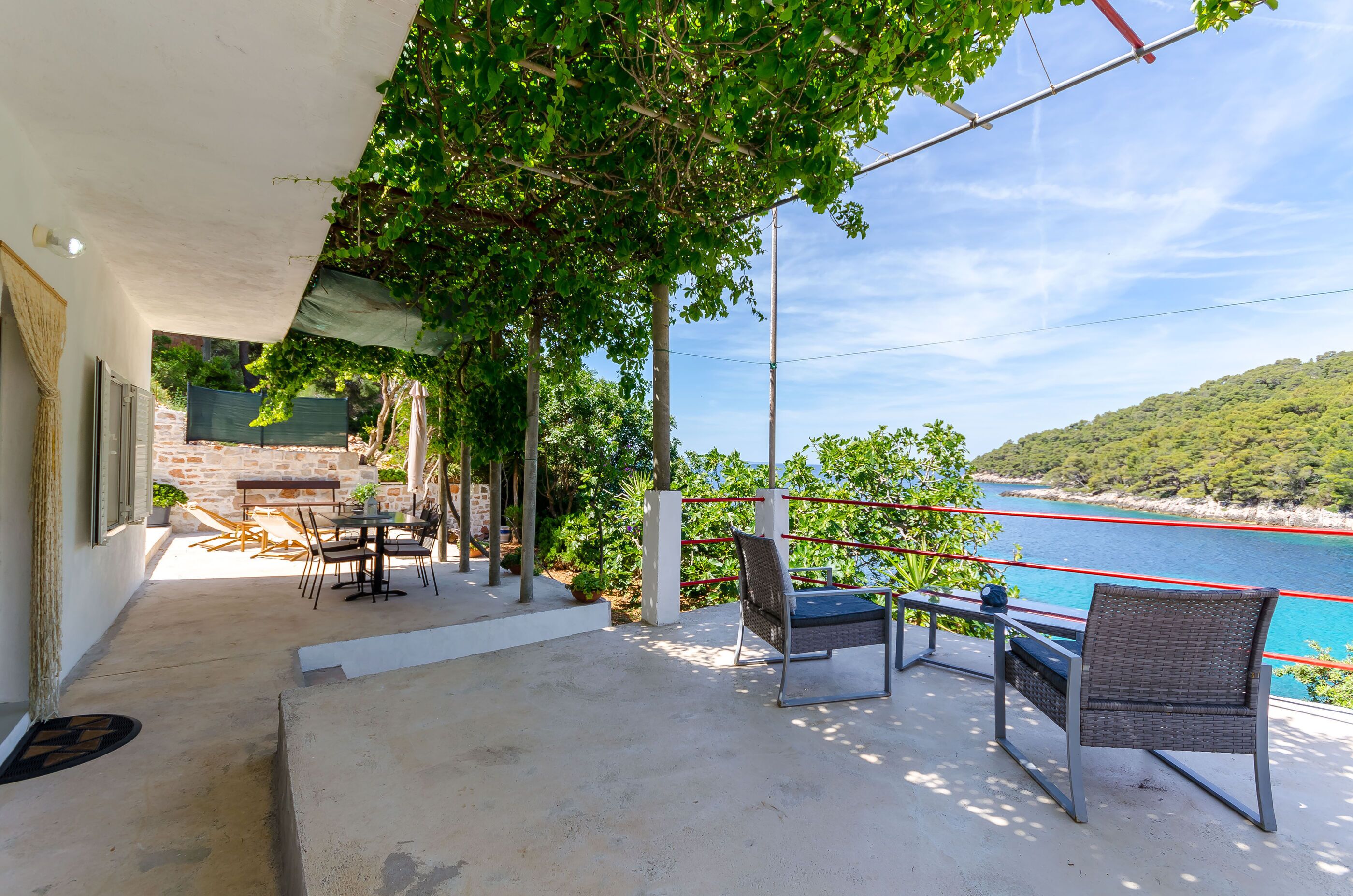 An outdoor patio with a table and chairs, a view of the sea, and a stone wall.