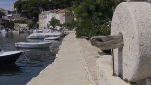 A marina with boats docked along a stone quay, surrounded by buildings and trees. - Apartments Soline (Podgora)
