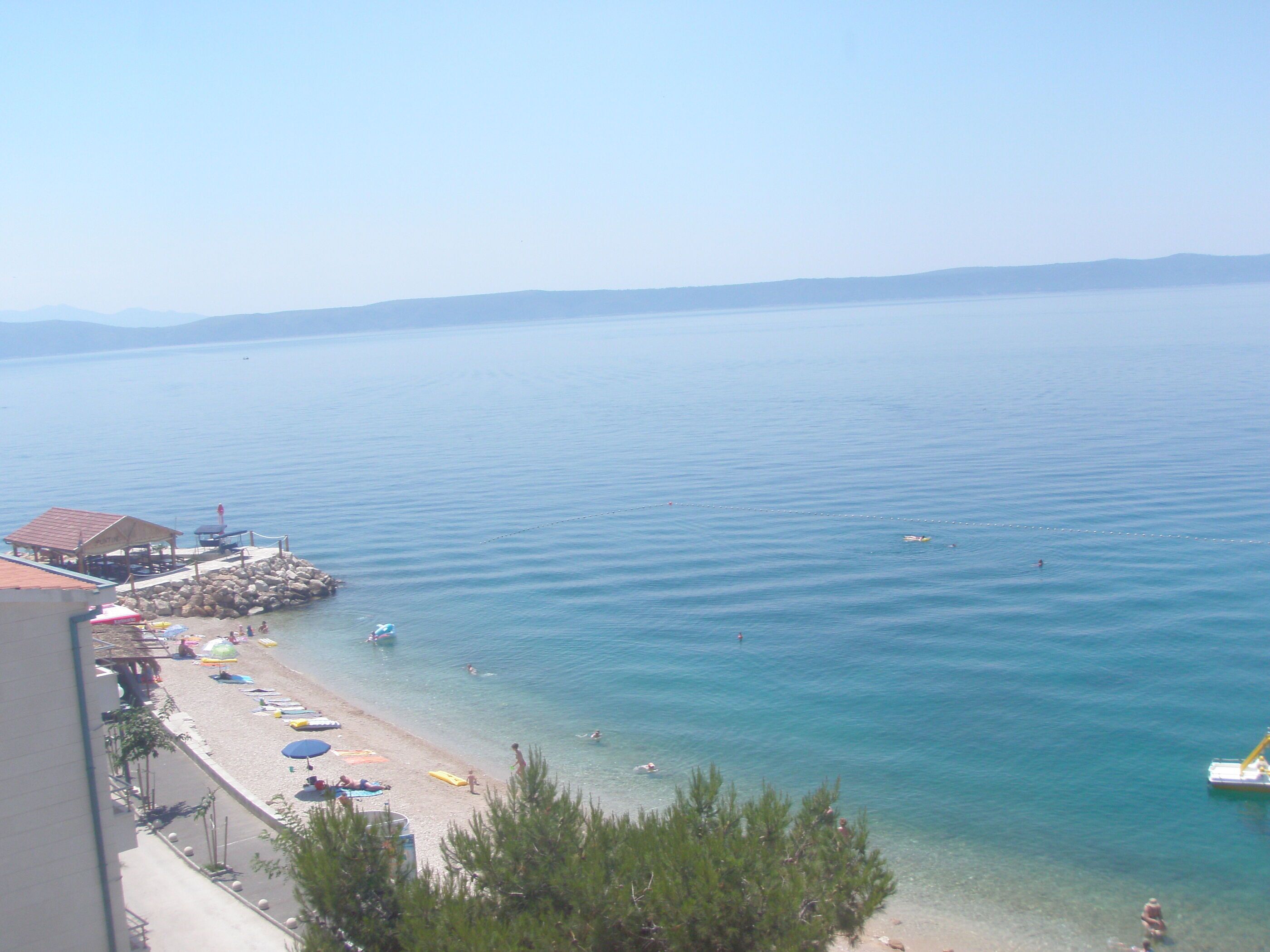 A beach with clear water, umbrellas, and a pier.