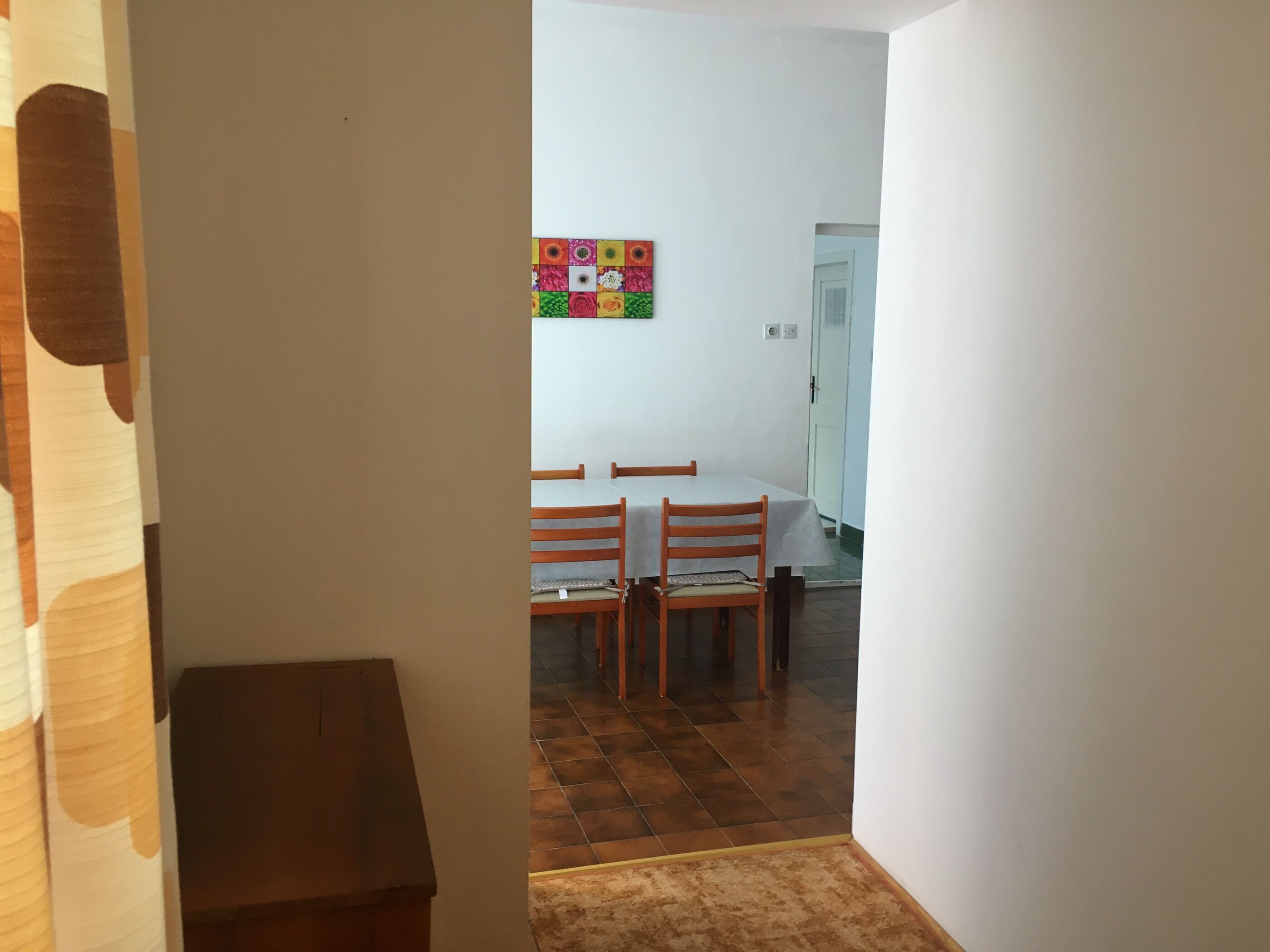 Corredor que leva a uma área de jantar, com piso ladrilhado e uma mesa com cadeiras.