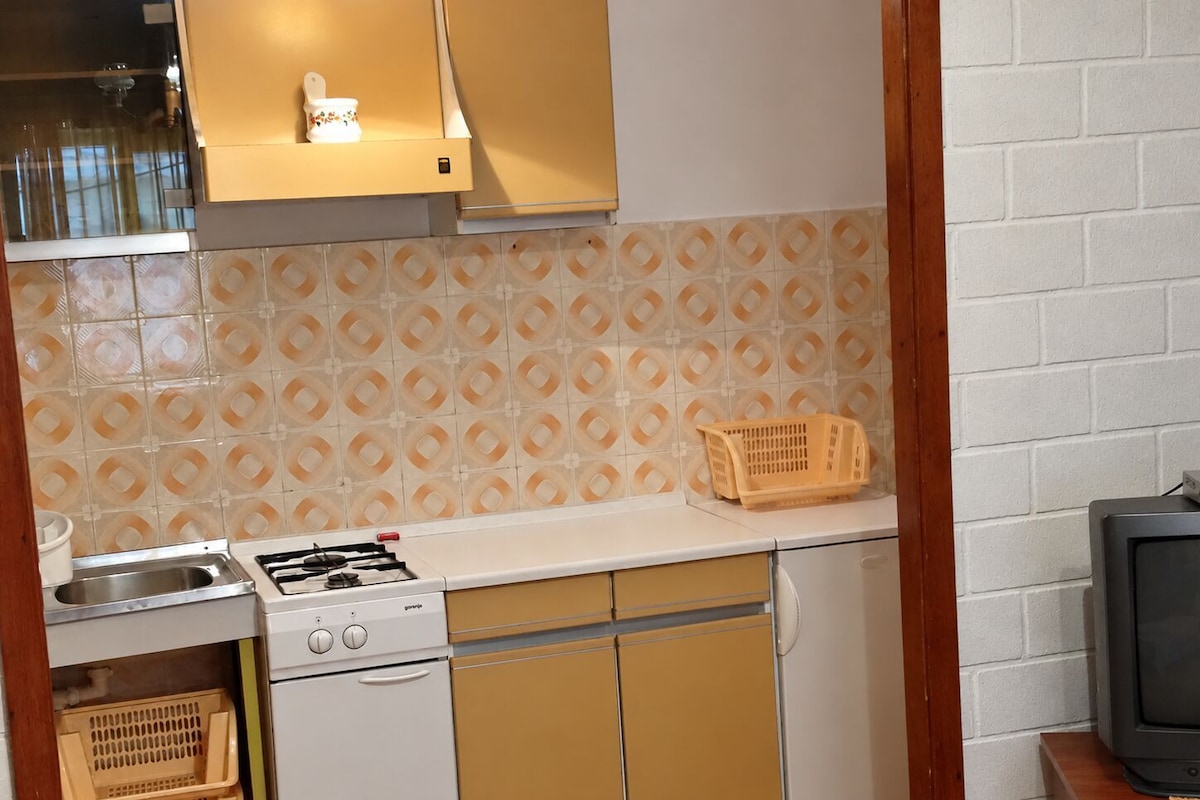 A compact kitchen with a gas stove, a sink, and a small television.