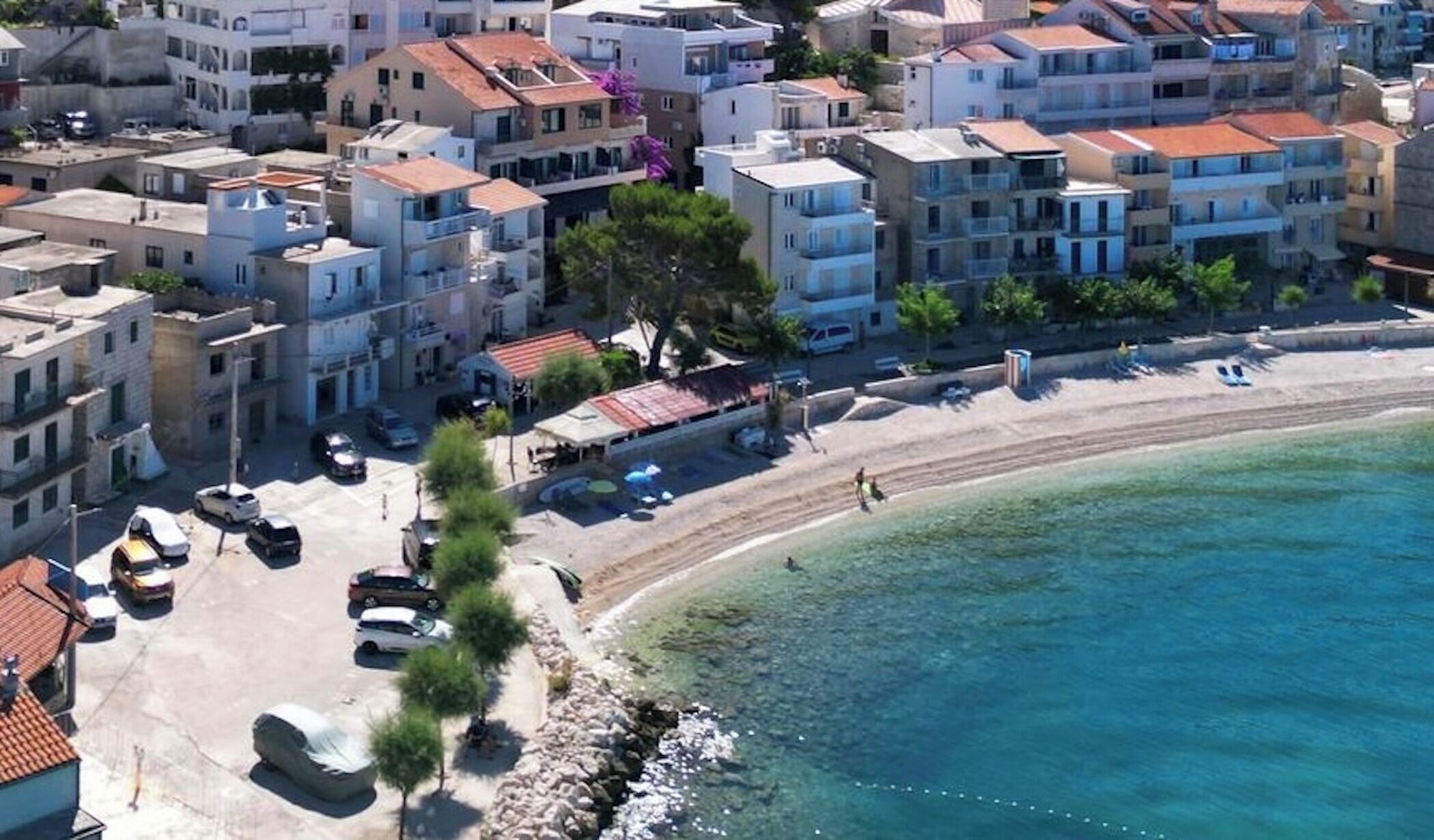 A coastal town with multi-story buildings, a sandy beach, and clear blue waters.