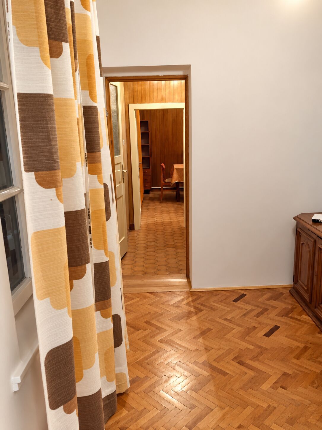 Ein Korridor mit Holzdielen im Fischgrätmuster, einem Holzschrank und einem Tisch mit Stühlen.
