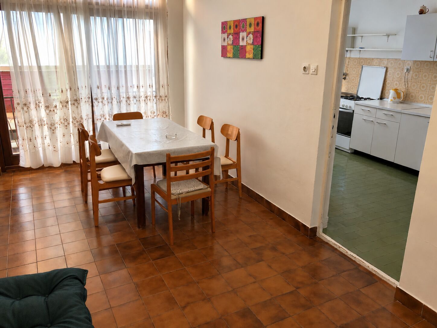 Un comedor con mesa y sillas, una cocina con armarios y una obra de arte colorida en la pared.
