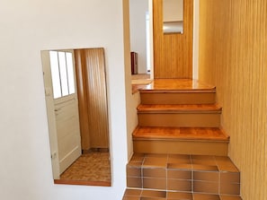 A narrow hallway with a wooden door and a small window, leading to a staircase with wooden steps and a tiled floor. - Apartments Soline (Podgora)