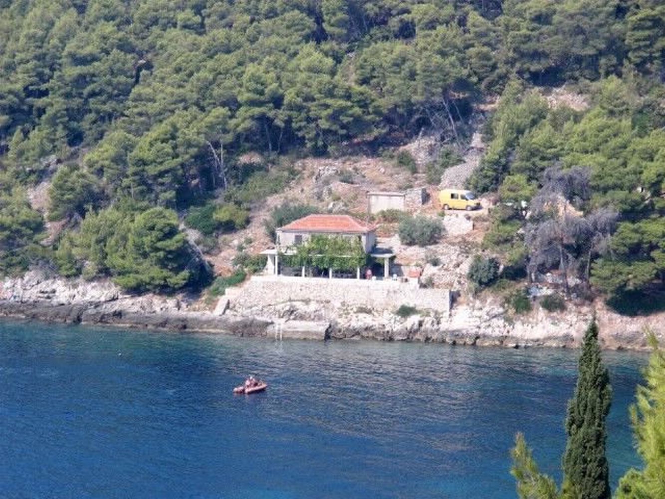 Una casa costera con techo rojo, ubicada en una costa rocosa con abundante vegetación de fondo.