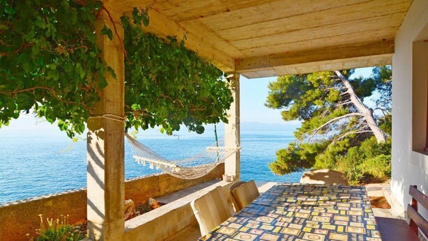 Ein überdachter Sitzbereich im Freien mit Blick auf das Meer, einer Hängematte und einer gemusterten Tischdecke.