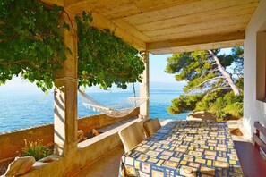Un espace extérieur abrité, aménagé avec des sièges, offrant une vue sur la mer, un hamac et une nappe  à motifs.