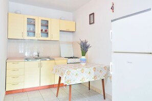Une cuisine avec des meubles de couleur jaune, un réfrigérateur blanc et une table recouverte d’une nappe à motifs floraux.