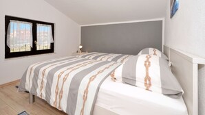 A bedroom with a bed, a nightstand, a lamp, and a window with curtains. - Apartments Petar (Rogoznica)