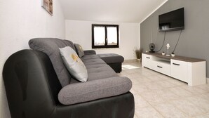A modern living room with a grey sofa, a flat-screen TV, and a minimalist white cabinet. - Apartments Petar (Rogoznica)