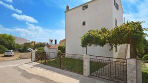 A white building with a stone gate, a tree in front, and a car parked nearby. - Apartments Petar (Rogoznica)