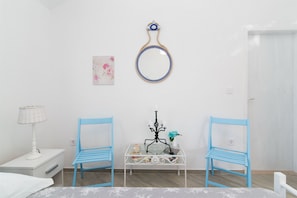 A room with a bed, a nightstand, a lamp, a blue chair, a small table with a book and a vase, and a wall-mounted mirror. - House Marija (Postira)