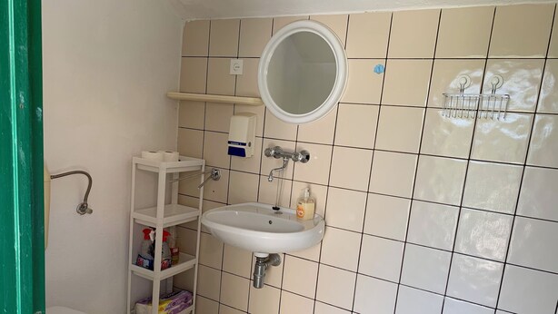 A bathroom with a white sink, a mirror, a toilet, and shelves with toiletries. - House Ivica (Postira)