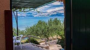 A patio with a view of a lake and mountains, a white plastic chair, and a wooden railing. - House Ivica (Postira)