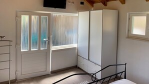 A bedroom with a wooden ceiling, a bed, a wardrobe, a TV mounted on the wall, and a window with frosted glass. - House Ivica (Postira)