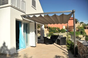 En overdækket terrasse med udendørs møbler, en skydedør og en stenvæg.