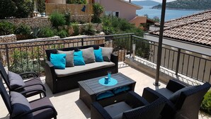 Ein Balkon mit Korbmöbeln, einer Steinmauer und Blick auf das Meer.