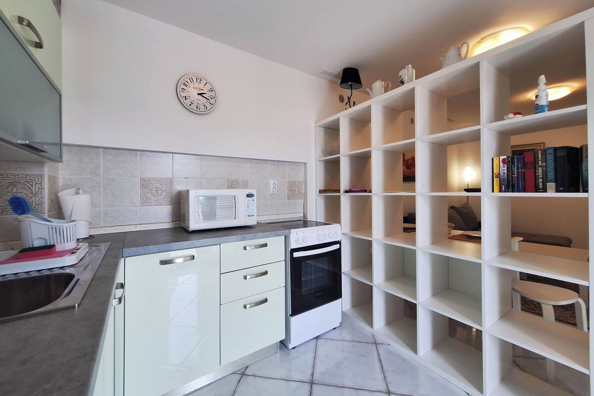 Eine moderne Küche mit weißen Schränken, einer Mikrowelle, einem Backofen und einer Uhr an der Wand.