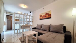 A living room with a sofa, a coffee table, and a dining area with a white cabinet and a painting on the wall. - Apartment Sofi (Crikvenica)
