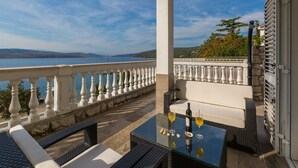 A balcony with a view of a lake and mountains, furnished with wicker chairs and a glass table with drinks. - Apartment Sofi (Crikvenica)