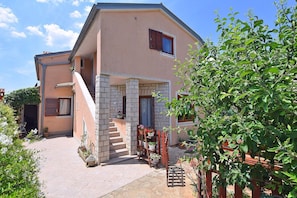 A two-story house with a stone staircase, a small porch with potted plants, and a garden area. - Apartments Petra (Fazana)