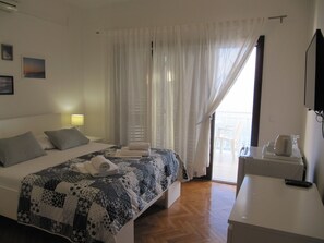 Een hotelkamer met een bed, nachtkastje, televisie en uitzicht op zee door het raam.