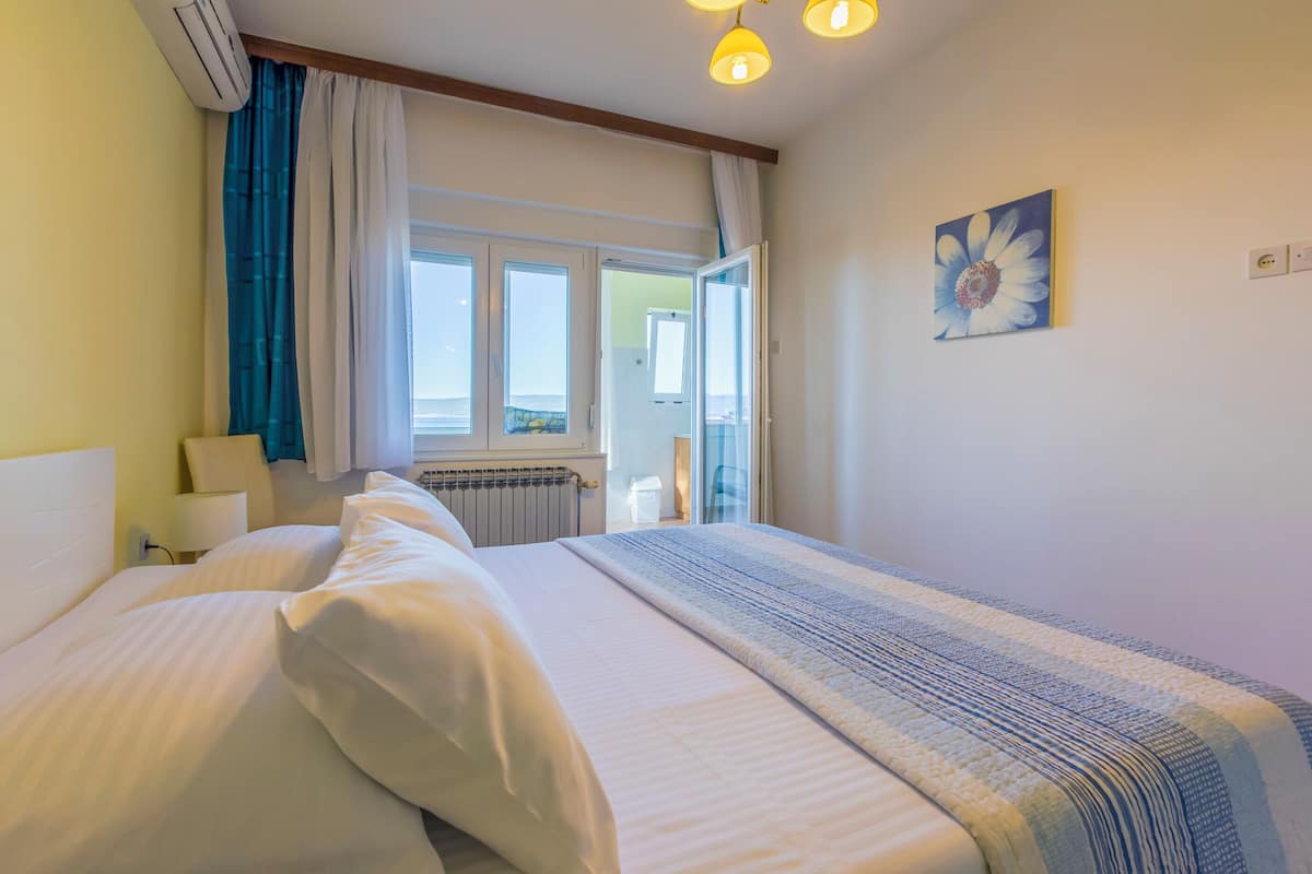 Une chambre d’hôtel avec un lit, une fenêtre avec des rideaux, un radiateur et un tableau au mur.