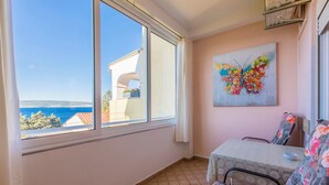 Ein Zimmer mit großem Fenster, das Meer- und Stadtblick bietet, einem Tisch mit einem blumigen Stuhl und einem farbenfrohen Schmetterlingsbild an der Wand.
