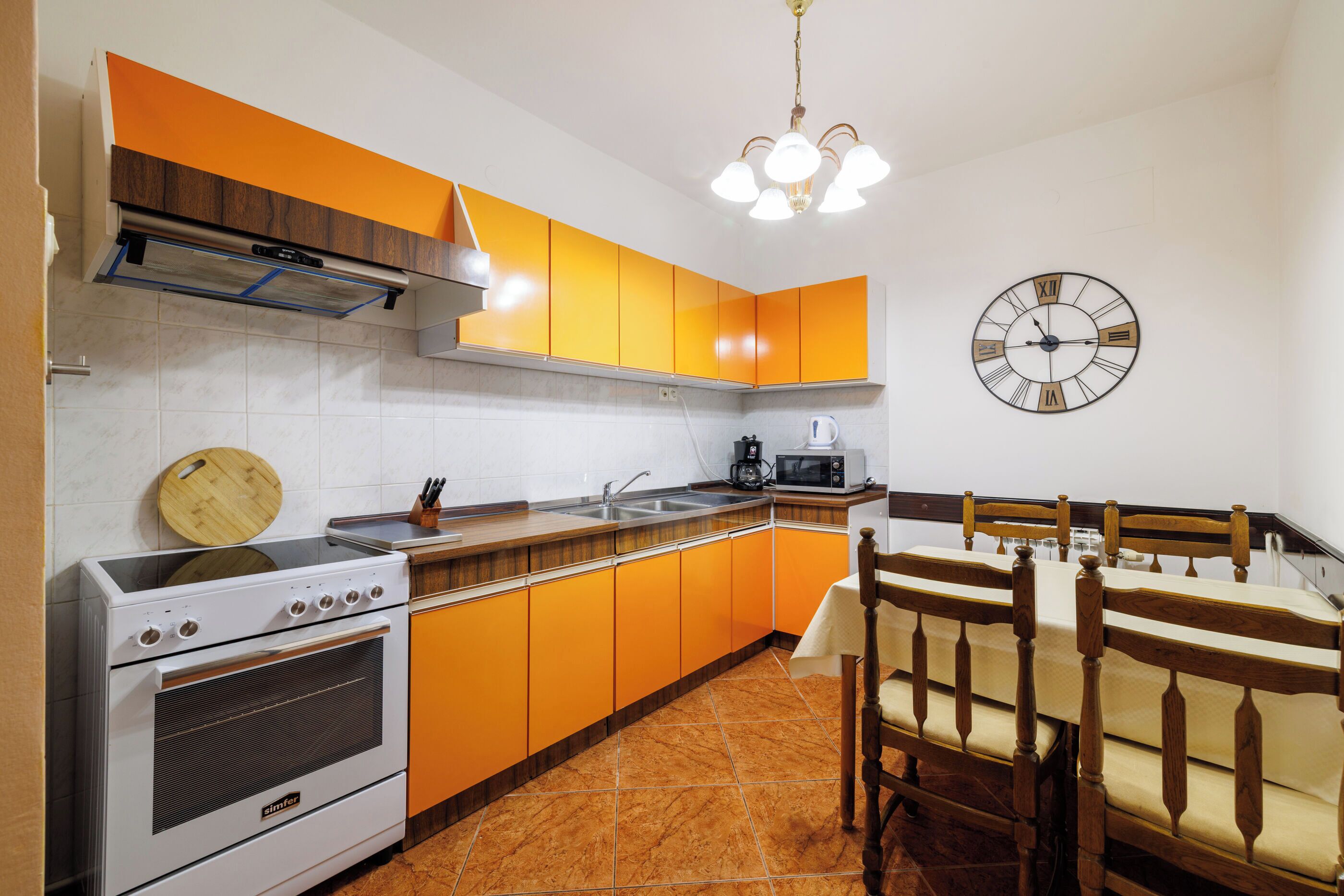 A kitchen with orange cabinets, a stove, a sink, and a dining area with a wooden table and chairs.