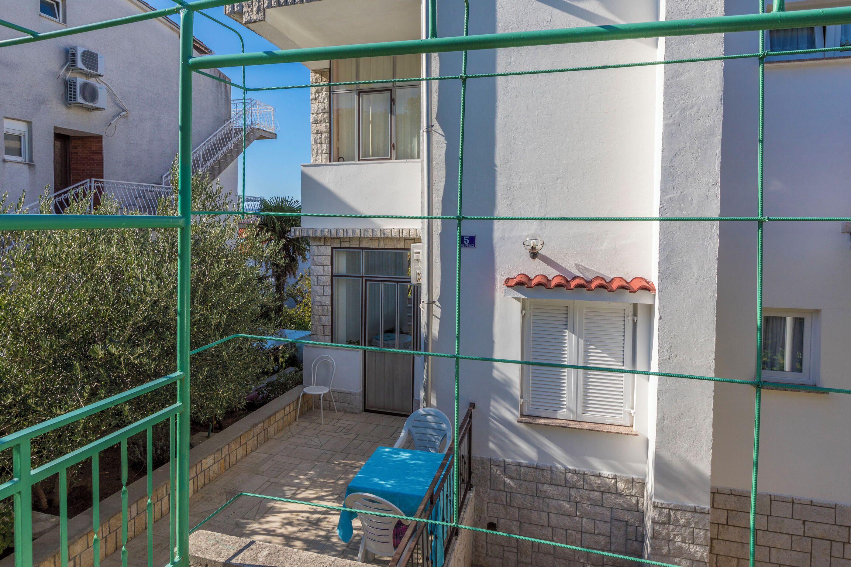 A courtyard with a blue table and chairs, a white building with a red-tiled roof, and a green metal fence.